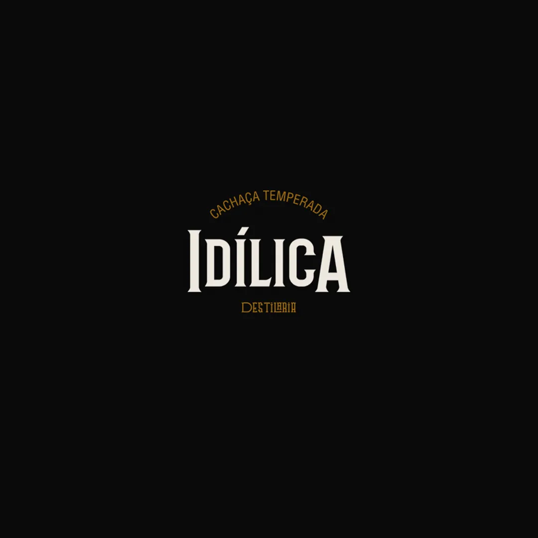 Logo escrito Cachaça Temperada Idílica Destilaria nas cores branco e dourado sobre fundo preto