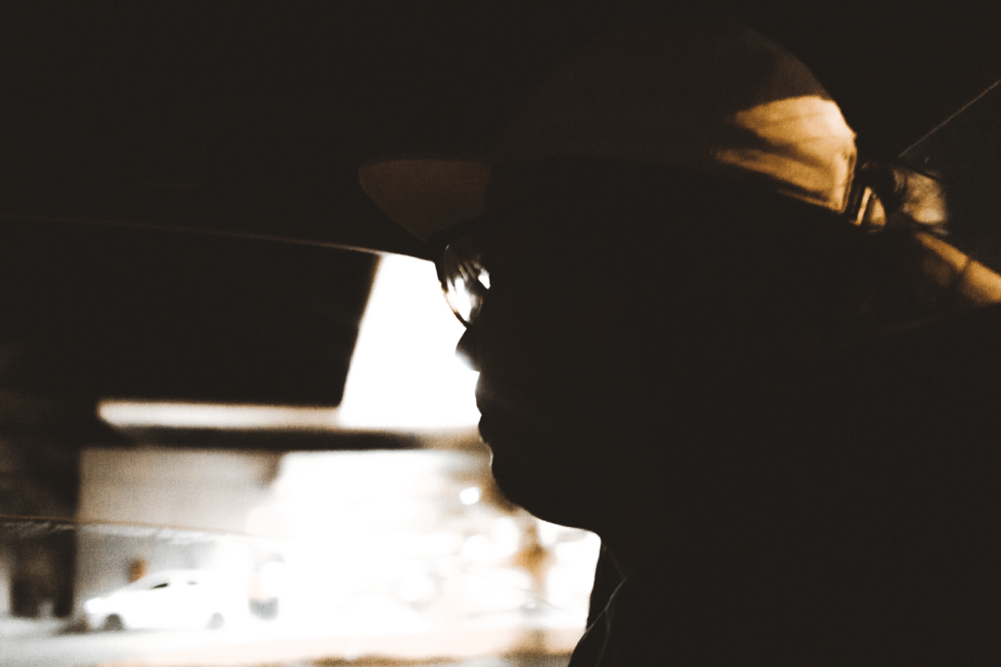 Nocturnal Silhouette Inside Car – Urban Portrait by Rodrigo Baumgratz In this moody, low-light urban portrait by Rodrigo Baumgratz, the silhouette of a man wearing glasses and a cap emerges subtly from the interior darkness of a car. A bright blur of artificial light cuts through the rear window, contrasting with the figure’s stillness and creating a composition rooted in tension, introspection, and urban solitude. The image reflects themes of anonymity, transit, and observation, offering a cinematic approach to documentary-style street photography. Perfect for portfolios focused on contemporary visual storytelling, low-key portraiture, and urban narrative fragments. Keywords: silhouette, night photography, man in car, low light, urban isolation, Rodrigo Baumgratz, street portrait.