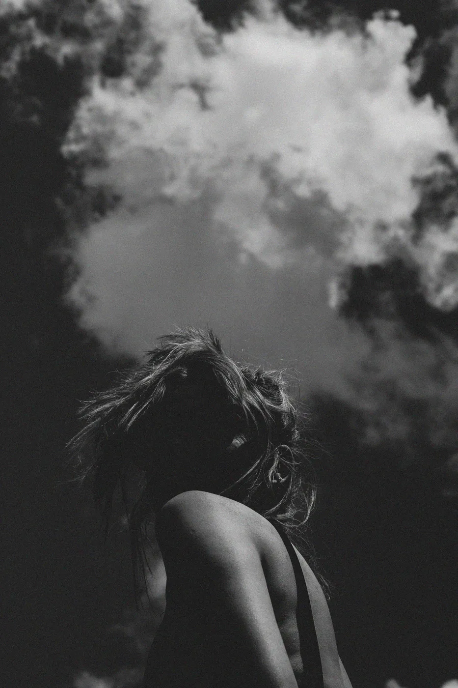 low angle of a photo of a woman. Half the image its her, the other half its a sky with clouds. Shot on black and white
