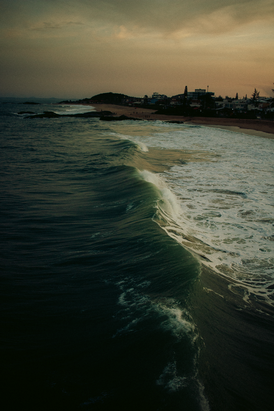 Coastal Landscape Photography at Sunset – Wave Breaking on Shoreline in Rio das Ostras by Rodrigo Baumgratz This atmospheric photograph by Rodrigo Baumgratz captures a dramatic wave rolling towards the shore in Rio das Ostras, under the fading light of sunset. The interplay between the dense textures of the water and the subtle pastel tones of the sky evokes a sense of quiet tension. Perfect for photography portfolios focused on coastal landscapes, light transitions, or contemplative nature, this image highlights motion, solitude, and the emotional resonance of the sea. Ideal for use in editorial, travel, or fine art collections.
