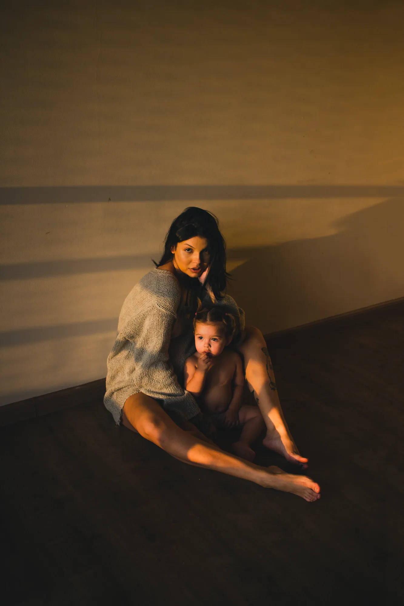 Mother and Child in Natural Light – Intimate Portraiture by Rodrigo Baumgratz Captured in black and white, this portrait explores the raw, quiet bond between a woman and child in a bare interior space. Rodrigo Baumgratz uses natural light and minimal composition to reveal vulnerability, strength, and emotional stillness—ideal for personal projects, editorial commissions, or campaigns exploring identity, motherhood, and domestic presence.