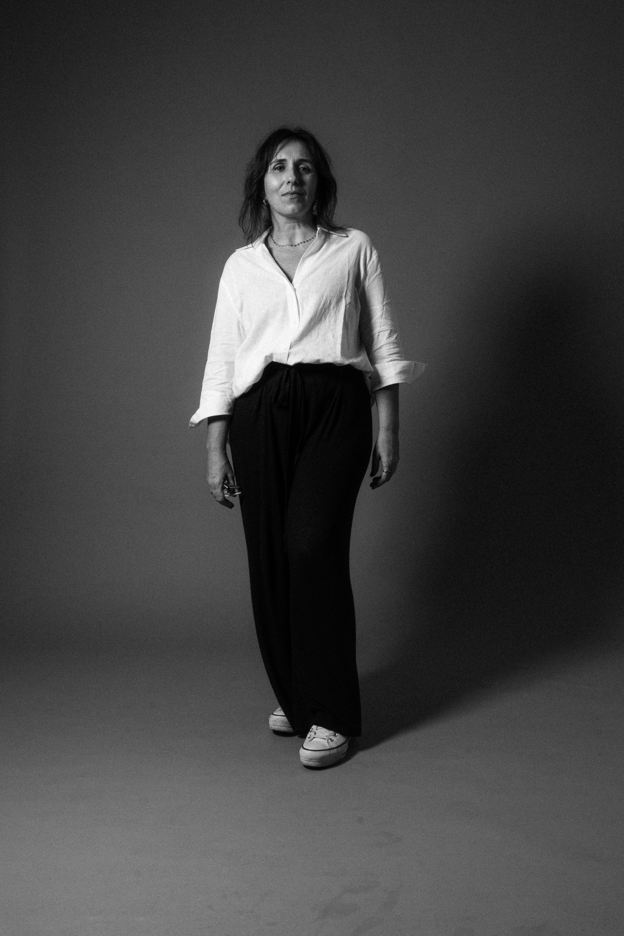Black and white shot of woman with a white blouse and black pants on a brown background. She is redhead, mature and seams tired but in control