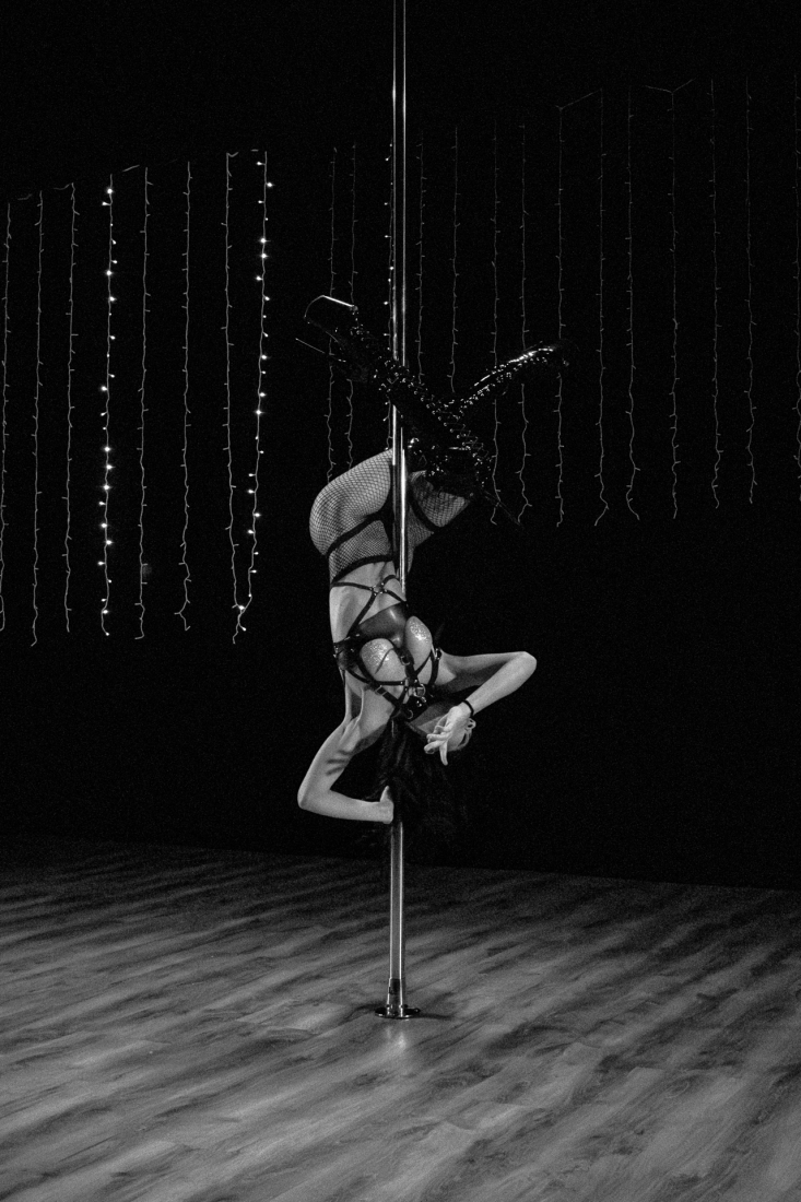 A black and white shot of a woman on a Pole Dance in the middle of a theater