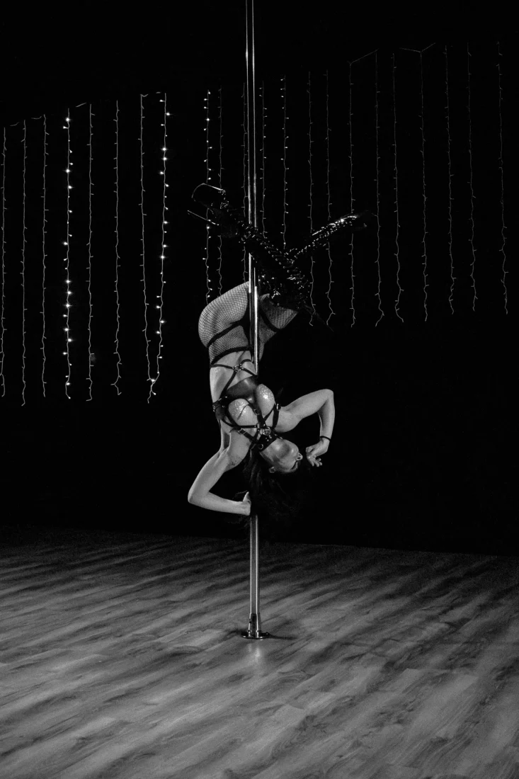 A black and white shot of a woman on a Pole Dance in the middle of a theater