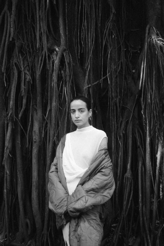 A Woman in the middle of huge roots with a white dress, green jacket and orange leggings