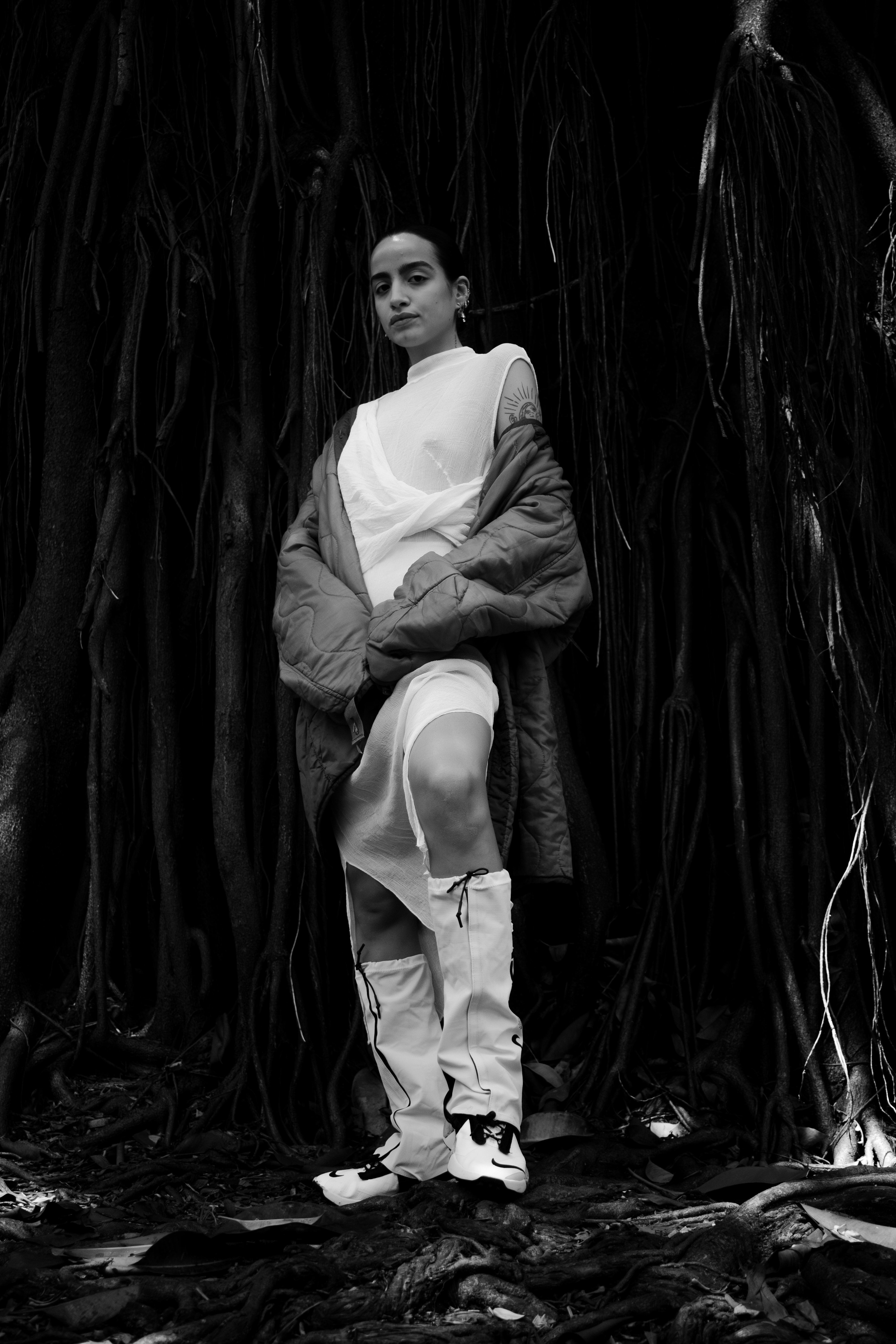 A Woman in the middle of huge roots with a white dress, green jacket and orange leggings