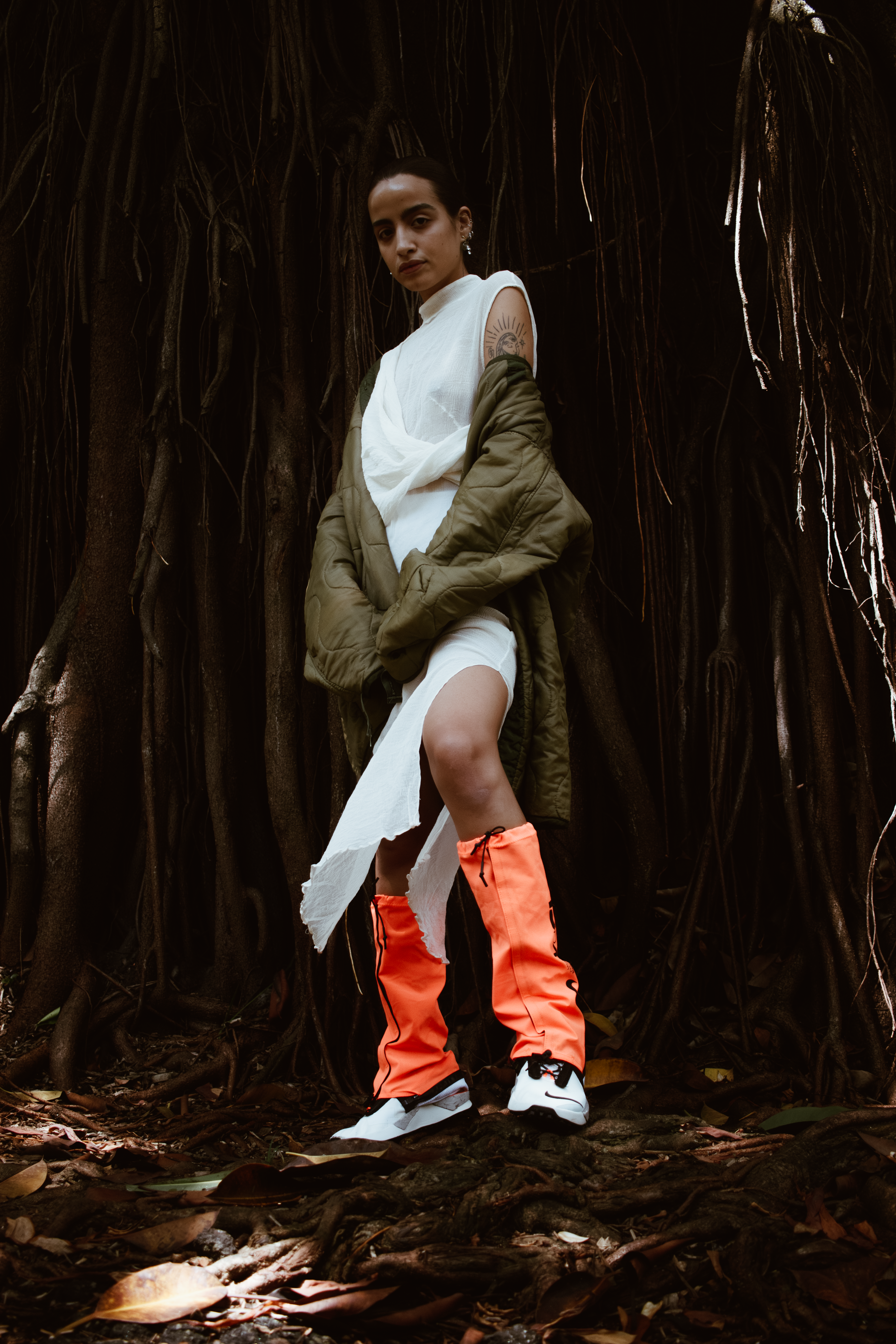 A Woman in the middle of huge roots with a white dress, green jacket and orange leggings