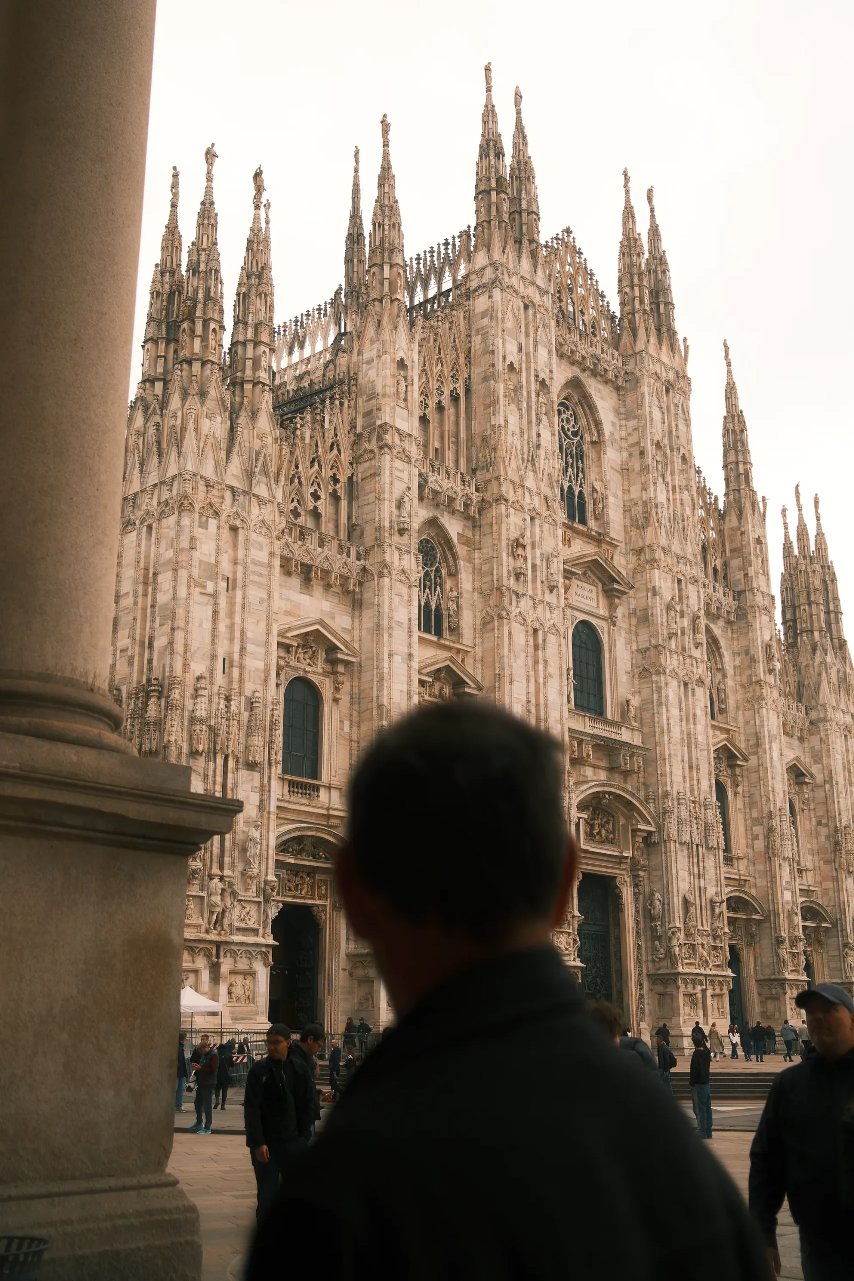 Gaze Toward the Duomo – Architectural Presence in Milan by Rodrigo Baumgratz In this evocative color photograph, the grandeur of Milan’s Duomo serves as a stage for human presence and perspective. A softly blurred figure in the foreground introduces scale, contemplation, and narrative depth against the cathedral’s intricate Gothic façade. With a cinematic approach to architectural storytelling, Rodrigo Baumgratz blends spatial design with emotional undertones—ideal for editorial, cultural, and commercial projects seeking poetic visual direction grounded in historical context.