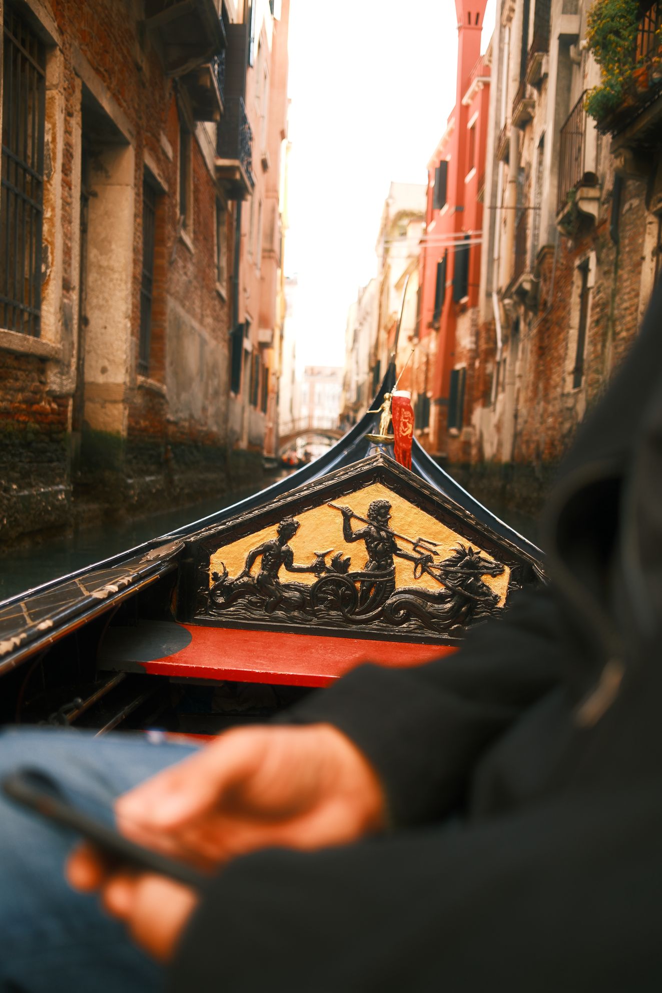 Venice Gondola Ride with Modern Gesture – Travel Photography This photograph by Rodrigo Baumgratz contrasts the timeless imagery of Venetian gondolas and mythic carvings with a modern intrusion: a passenger’s hand holding a phone. It reflects the coexistence of history and contemporary habits in the same fleeting moment.