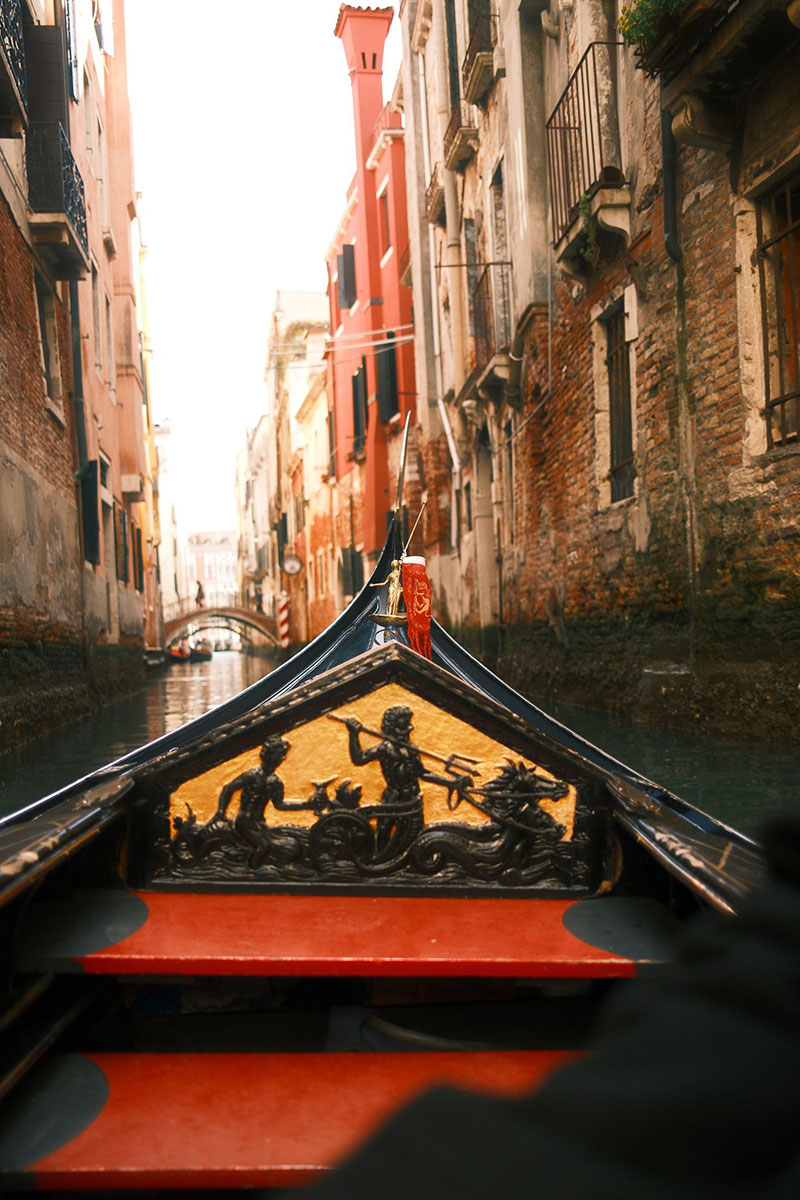 Venice Narrow Canal Gondola Ride – Intimate Cityscape Photography Rodrigo Baumgratz captures the intimate side of Venice, where gondolas glide through narrow canals lined with weathered façades. The prow’s carved detail, depicting mythic figures, becomes a reminder of the city’s timeless relationship with water and legend.
