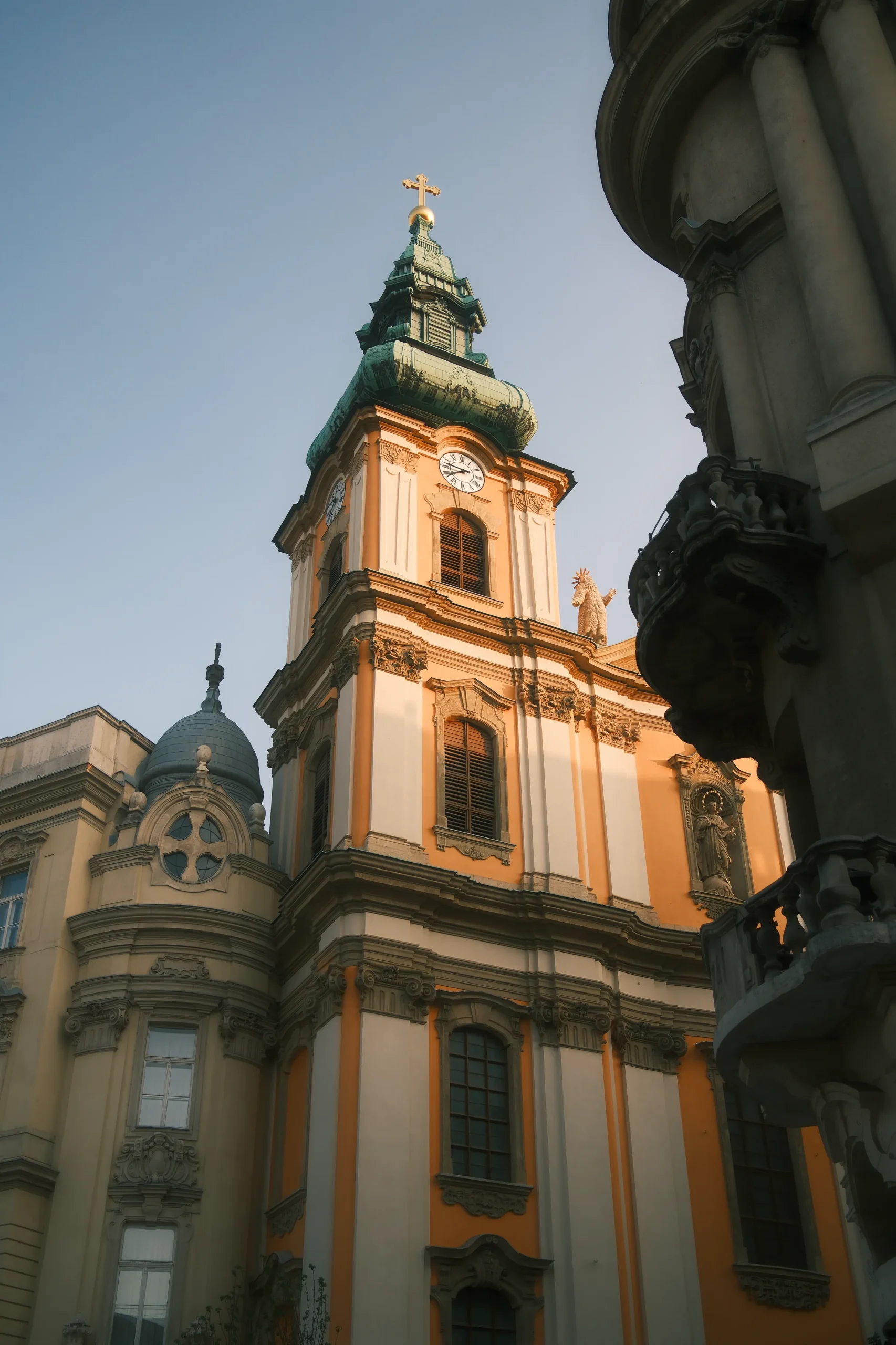 Architectural photograph of an ornate Baroque church in Budapest, captured in warm afternoon light with twin towers and green copper roofs. Creative director portfolio photography focused on historic architecture and visual composition.